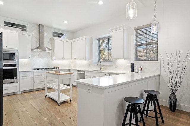 kitchen featuring stainless steel appliances, wall chimney range hood, a sink, and white cabinetry