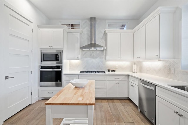 kitchen featuring white cabinets, wall chimney exhaust hood, butcher block countertops, and stainless steel appliances