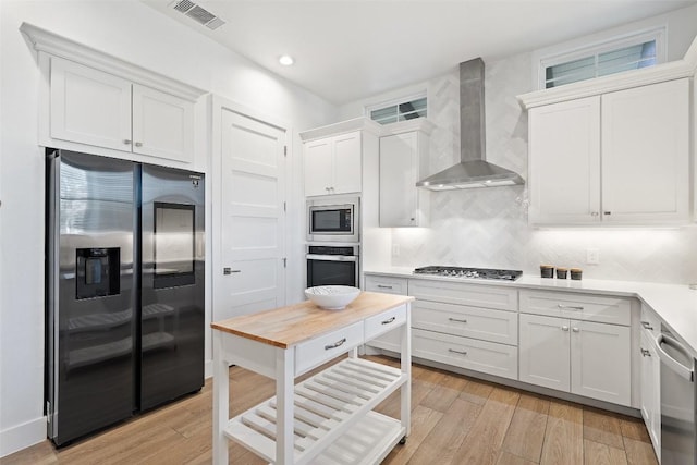 kitchen with white cabinets, wall chimney range hood, visible vents, and stainless steel appliances