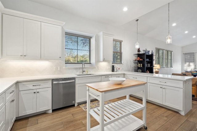 kitchen featuring a peninsula, a sink, dishwasher, light wood finished floors, and tasteful backsplash