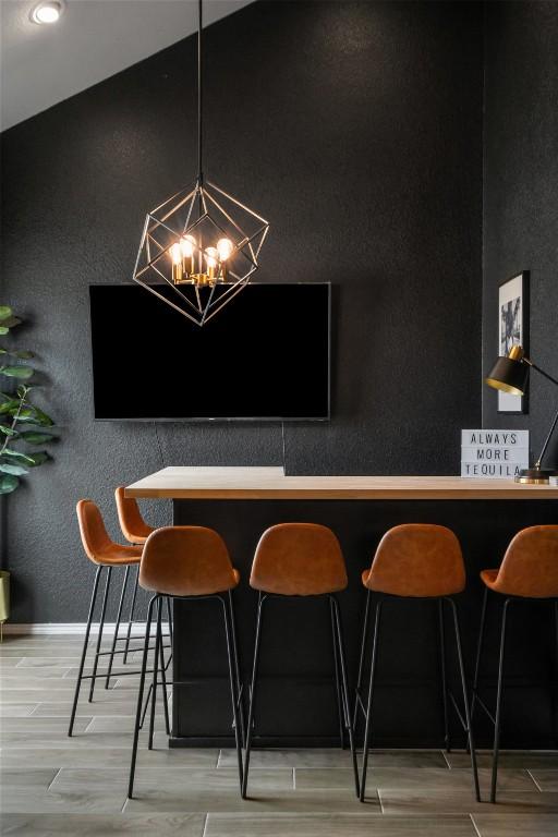 bar with baseboards, a textured wall, wood finished floors, and a notable chandelier