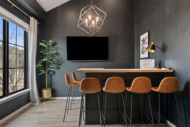 bar with a dry bar, baseboards, a textured wall, an inviting chandelier, and wood tiled floor