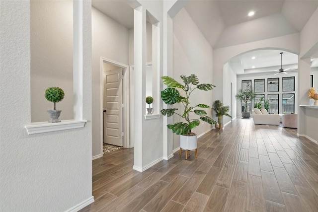 hallway featuring arched walkways, recessed lighting, a high ceiling, baseboards, and wood tiled floor