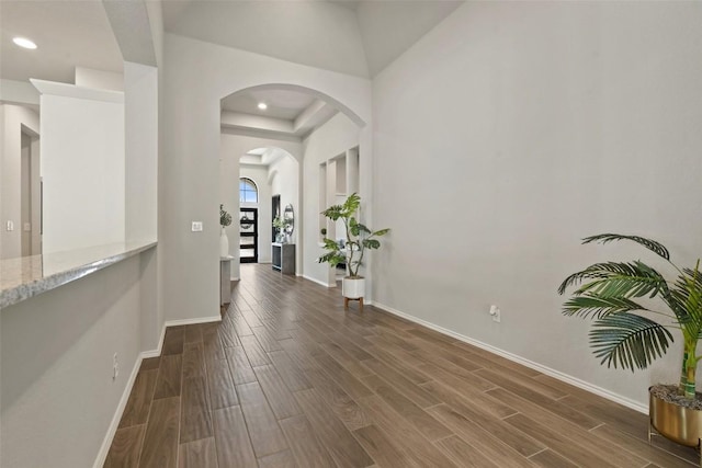 hall featuring wood finish floors, arched walkways, baseboards, and recessed lighting