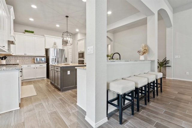 kitchen featuring arched walkways, stainless steel appliances, white cabinets, decorative backsplash, and wood tiled floor