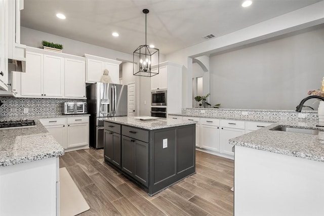 kitchen with visible vents, white cabinets, wood tiled floor, stainless steel appliances, and a sink