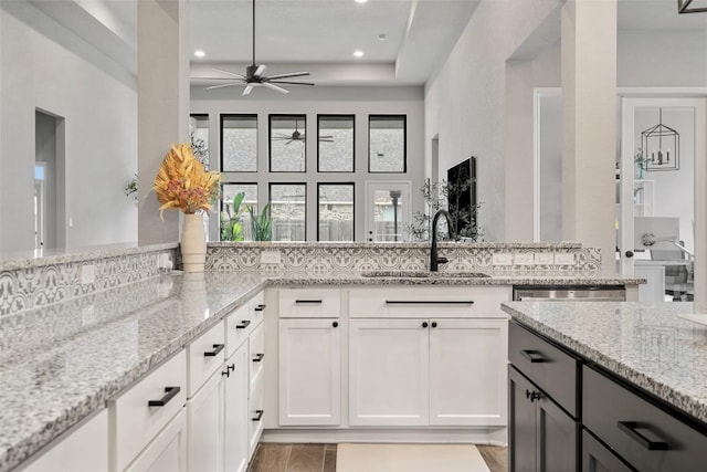 kitchen with light stone counters, a peninsula, white cabinetry, a sink, and recessed lighting