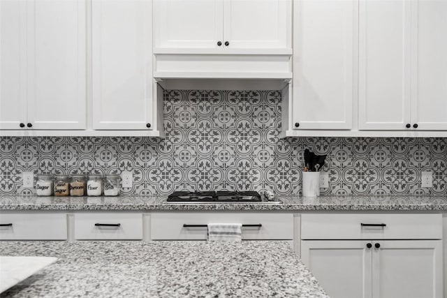 kitchen featuring tasteful backsplash, white cabinets, stainless steel gas cooktop, and light stone counters