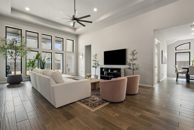 living area with dark wood-style floors, a tray ceiling, a high ceiling, ceiling fan, and baseboards