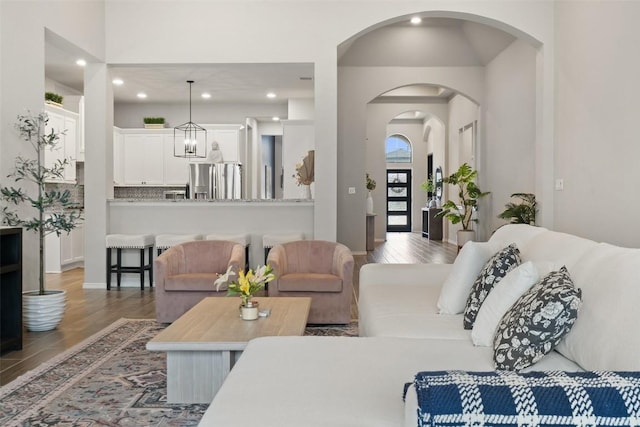 living area featuring arched walkways, recessed lighting, wood finished floors, and a notable chandelier