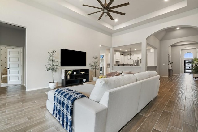 living area with arched walkways, a high ceiling, wood finish floors, and a ceiling fan