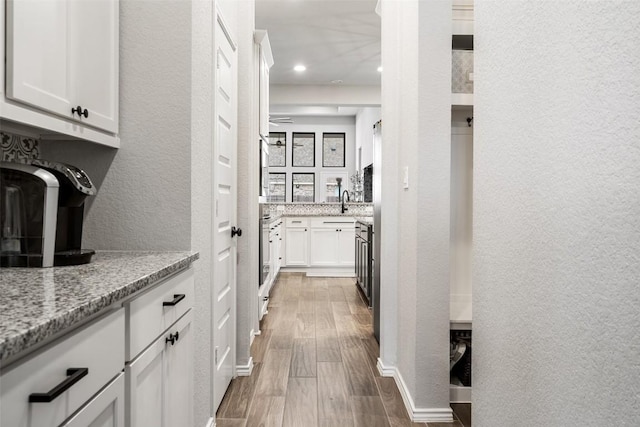 kitchen featuring a textured wall, wood finished floors, light stone countertops, white cabinetry, and a sink