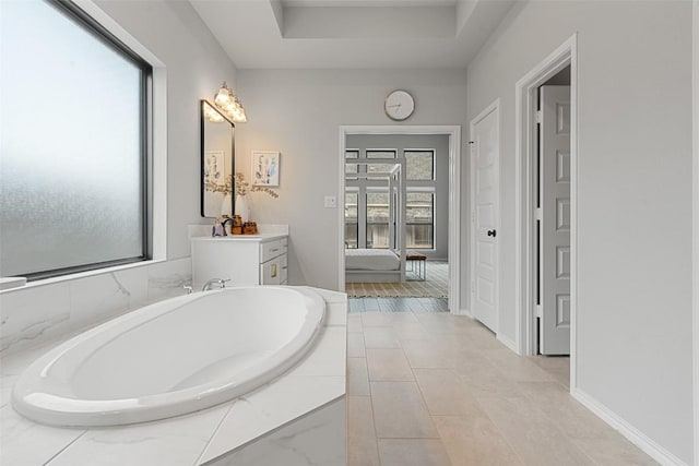 bathroom with baseboards, a raised ceiling, a bath, and vanity