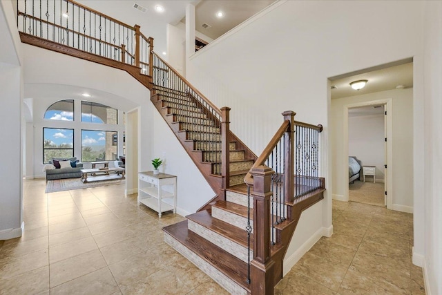 staircase featuring a high ceiling, visible vents, and baseboards