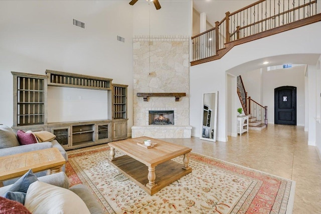 living room with a ceiling fan, a stone fireplace, visible vents, and stairway