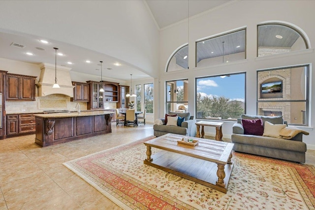 living room with light tile patterned floors, visible vents, a towering ceiling, ornamental molding, and a lit fireplace