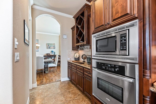 kitchen with arched walkways, decorative backsplash, light stone counters, ornamental molding, and stainless steel appliances