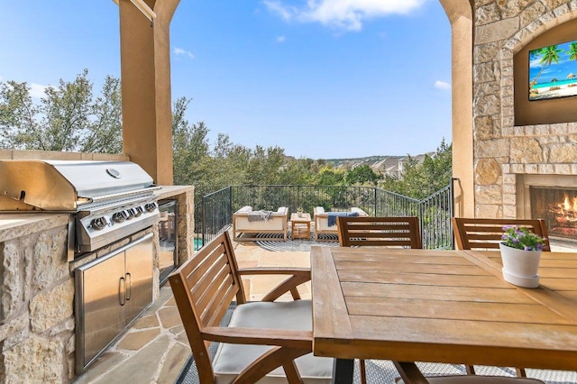 balcony with an outdoor kitchen, a patio, area for grilling, an outdoor stone fireplace, and outdoor dining space