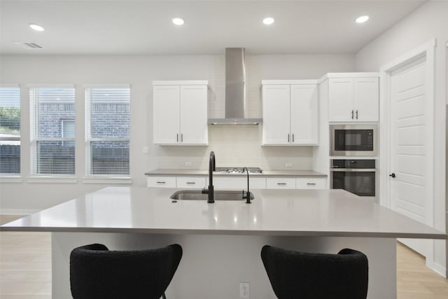 kitchen featuring stainless steel appliances, light countertops, visible vents, a sink, and wall chimney exhaust hood