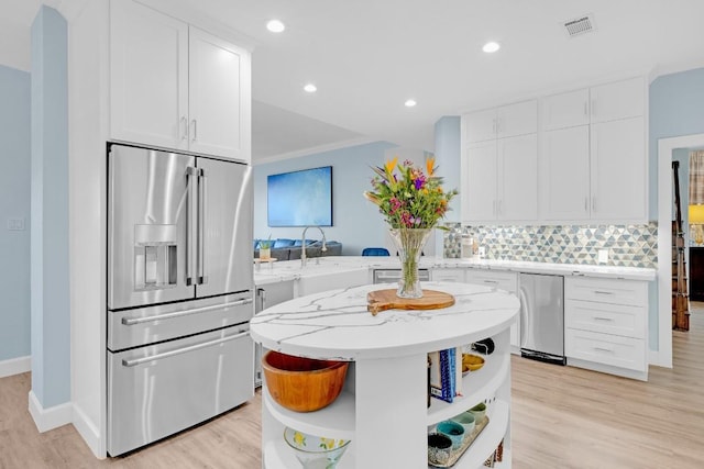 kitchen with a sink, white cabinets, open shelves, tasteful backsplash, and stainless steel fridge