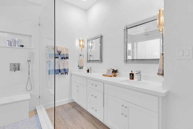 bathroom with double vanity, a walk in shower, a sink, and wood finished floors