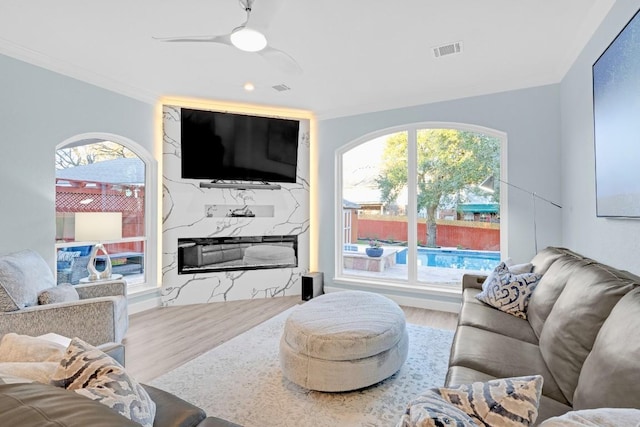 living room featuring visible vents, a ceiling fan, ornamental molding, wood finished floors, and a fireplace