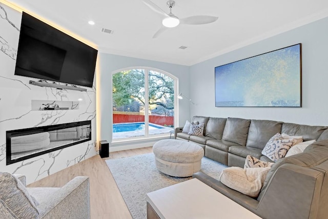 living area with ceiling fan, wood finished floors, visible vents, a high end fireplace, and crown molding