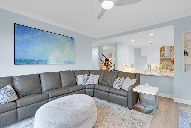 living room with crown molding, ceiling fan, light wood-type flooring, baseboards, and stairs