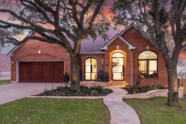 view of front of house with brick siding, roof with shingles, concrete driveway, a front yard, and a garage