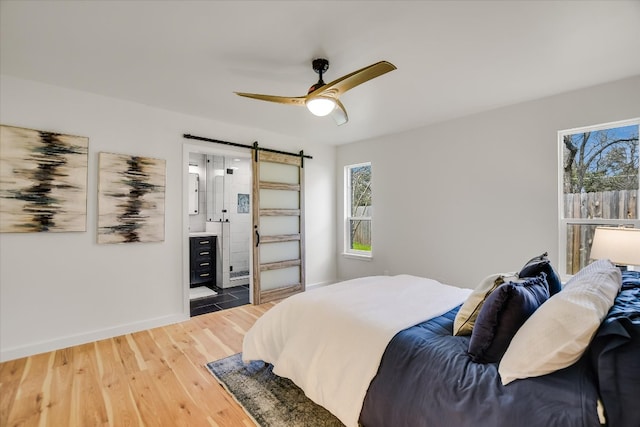 bedroom featuring a barn door, baseboards, a ceiling fan, ensuite bath, and light wood-style floors