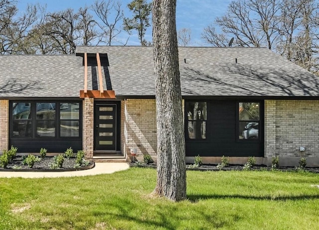 back of property featuring a yard, a shingled roof, and brick siding