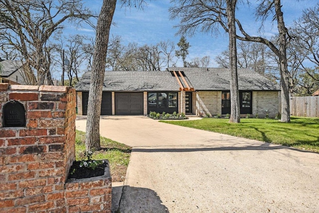 mid-century inspired home with a garage, concrete driveway, fence, a front lawn, and brick siding