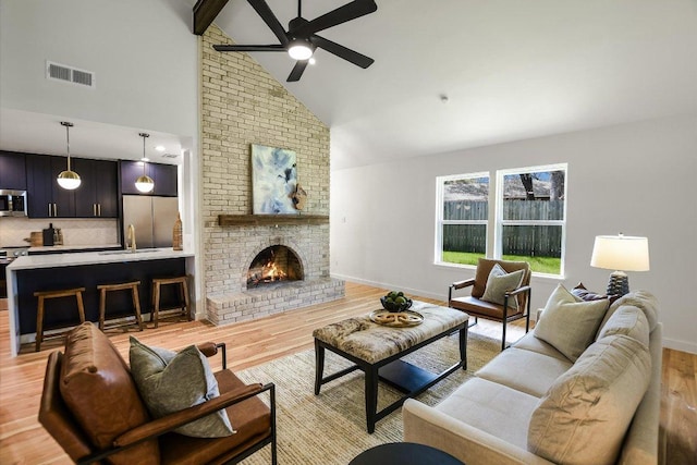 living area with high vaulted ceiling, light wood-type flooring, visible vents, and a fireplace