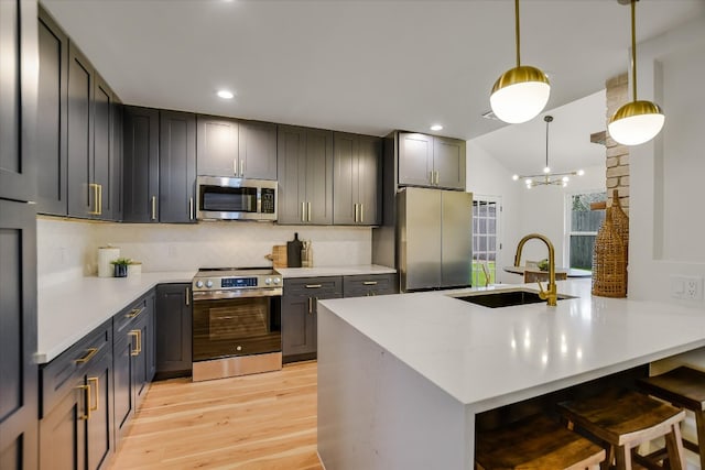 kitchen featuring stainless steel appliances, light countertops, light wood-style floors, a sink, and a kitchen bar