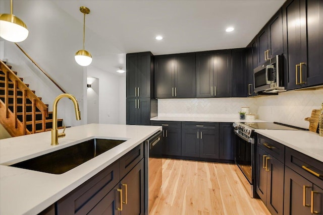 kitchen featuring light wood-style flooring, appliances with stainless steel finishes, light countertops, pendant lighting, and a sink