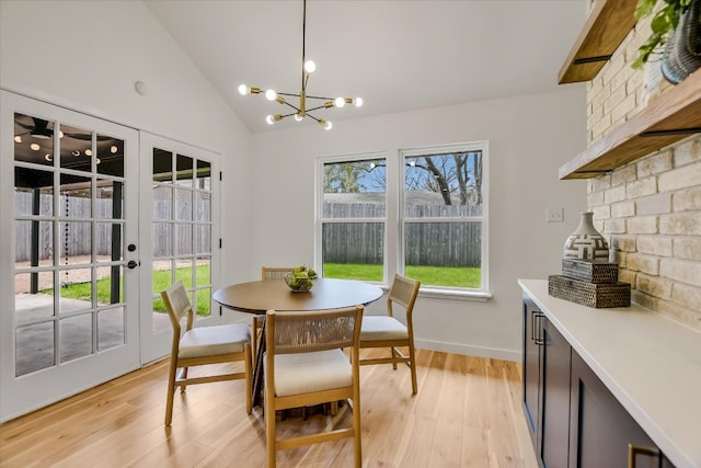 dining area with a notable chandelier, baseboards, vaulted ceiling, light wood-style floors, and french doors