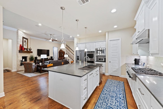 kitchen with stainless steel appliances, visible vents, backsplash, a stone fireplace, and wood finished floors