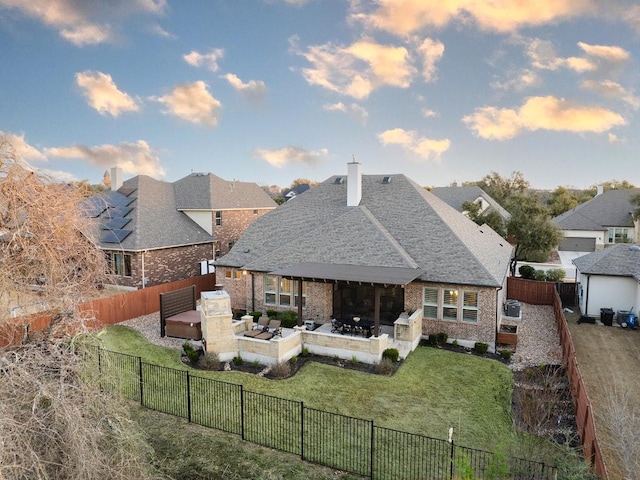 rear view of property with brick siding, a chimney, a lawn, a patio area, and a fenced backyard