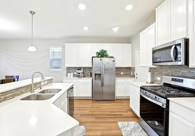 kitchen featuring white cabinets, appliances with stainless steel finishes, light countertops, light wood-type flooring, and a sink