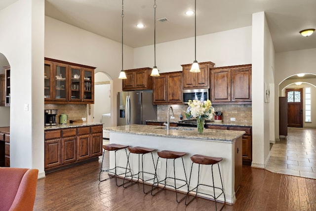 kitchen featuring arched walkways, stainless steel appliances, a sink, and a kitchen breakfast bar