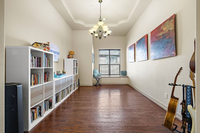 interior space featuring a chandelier, a raised ceiling, baseboards, and wood finished floors