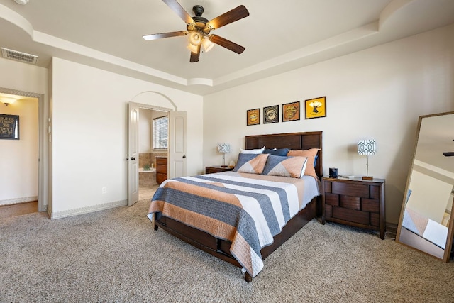 carpeted bedroom featuring a raised ceiling, visible vents, a ceiling fan, connected bathroom, and baseboards