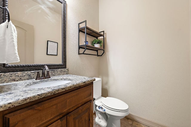 half bath with toilet, a textured wall, baseboards, and vanity