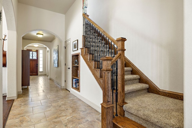 entryway featuring arched walkways, stone finish flooring, a high ceiling, and baseboards