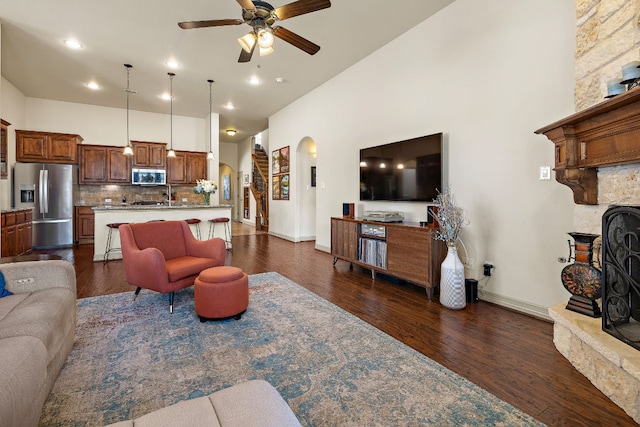 living room featuring arched walkways, a towering ceiling, dark wood-style floors, ceiling fan, and a fireplace