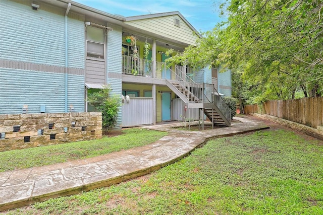 rear view of house with a yard, fence, and stairs