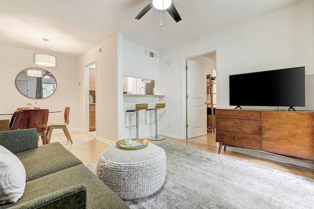 living room with light wood-style floors, visible vents, ceiling fan, and baseboards