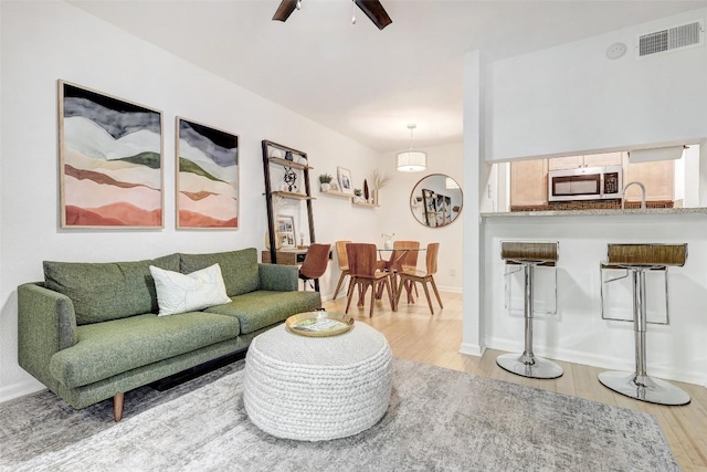 living area with baseboards, light wood-style flooring, visible vents, and a ceiling fan