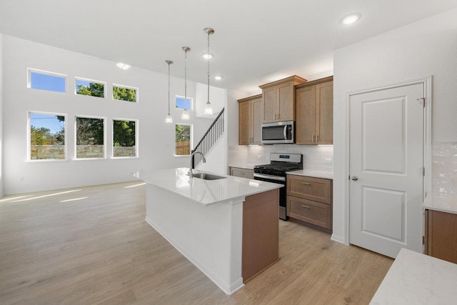 kitchen with stainless steel appliances, a sink, light wood finished floors, brown cabinetry, and tasteful backsplash