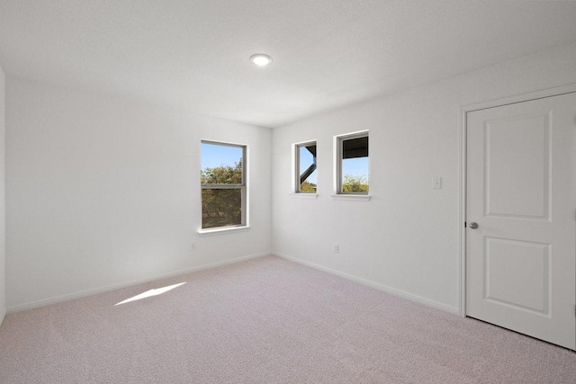 unfurnished room with baseboards and light colored carpet